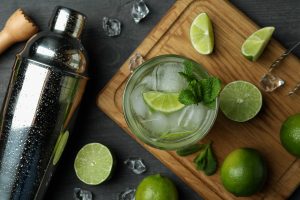 Glass of mojito cocktail, ingredients and shaker on dark wooden background