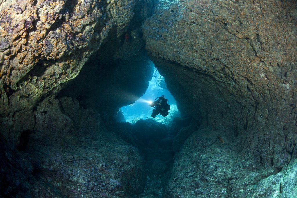 Scuba Diver with LIght Enters Coral Cavern