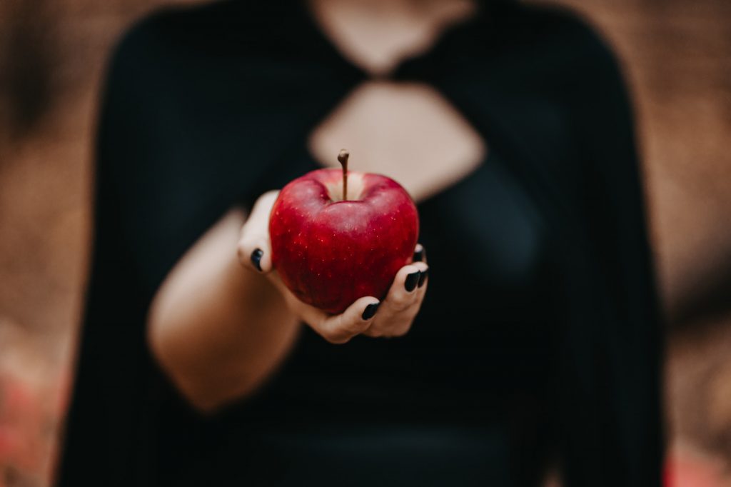 Woman as witch offers red apple as symbol of temptation, poison. Fairy tale, halloween, cosplay.