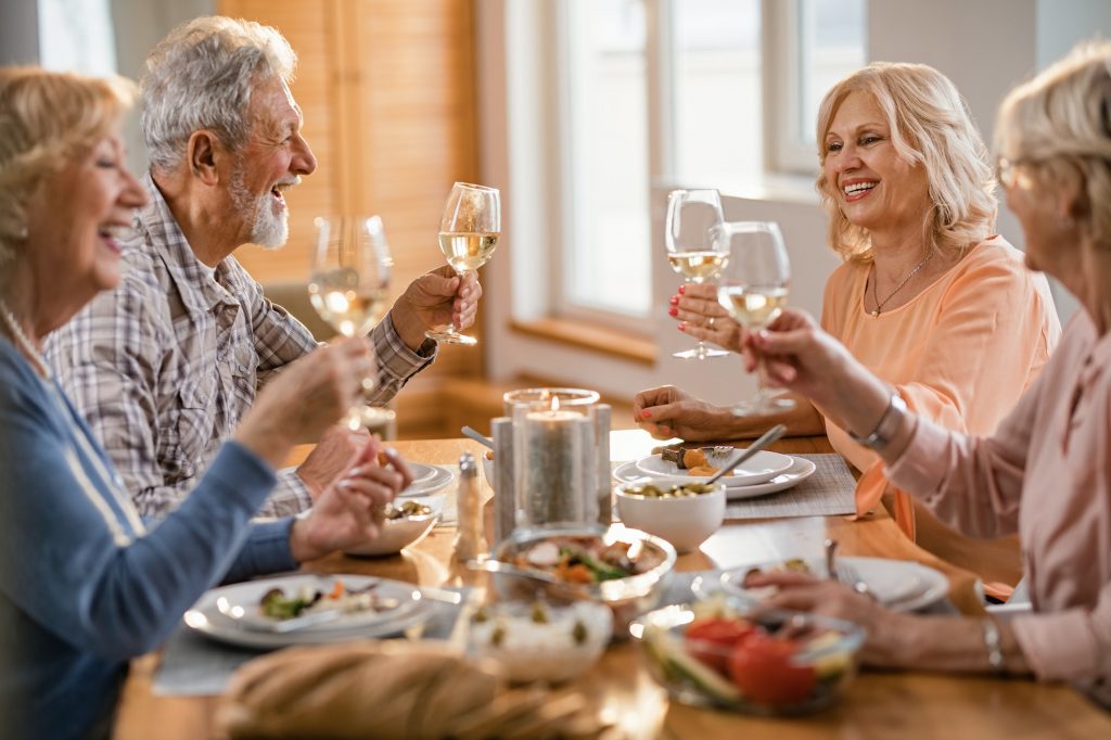 Cheerful mature people toasting with wine while having lunch at home.