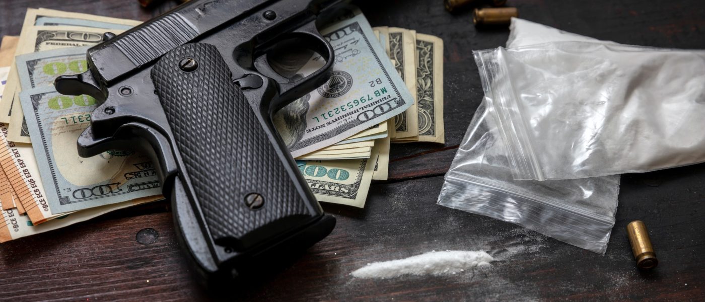 Drugs narcotics business concept. Cocaine plastic packets, gun and US dollars banknotes on a table.