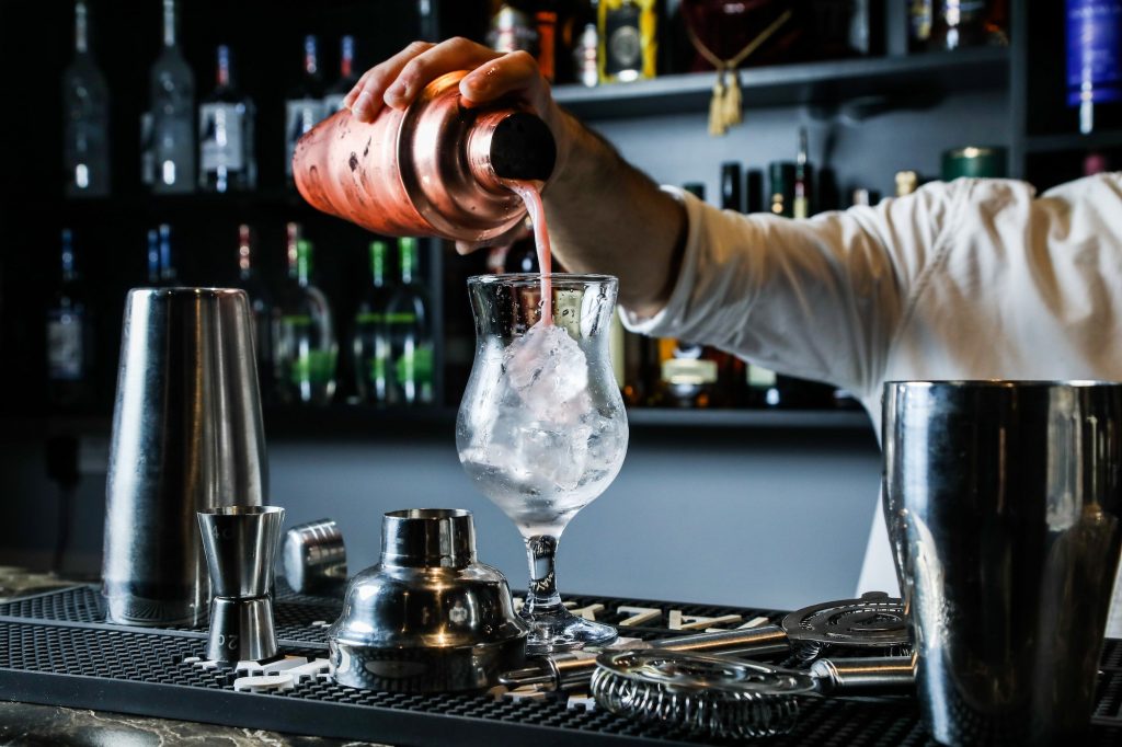 man pouring cocktail from shaker in the glass with ice bar side view