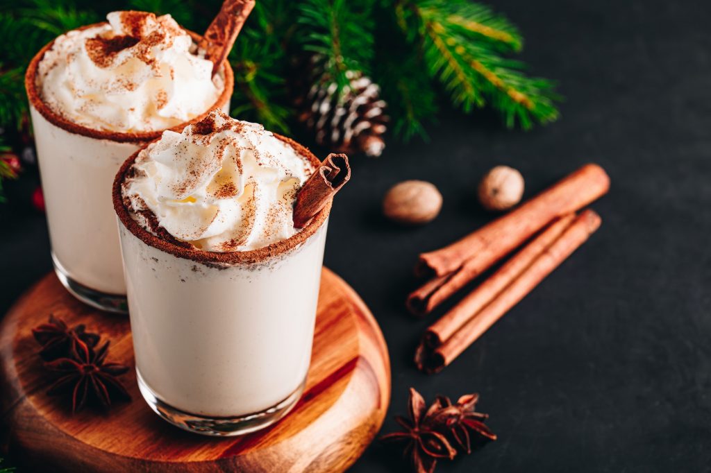 Traditional Christmas drink Eggnog with whipped cream and cinnamon on dark stone background.