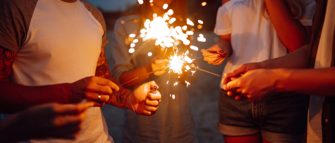 Group of people holding sparklers at party on the beach. Young friends have fun with fire sparkles.