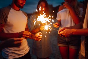 Group of people holding sparklers at party on the beach. Young friends have fun with fire sparkles.