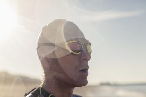 A swimmer in a wet suit, swimming hat and goggles on a beach.