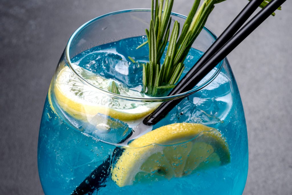 Alcoholic cocktail blue curacao with ice, lemon and cocktail tubes