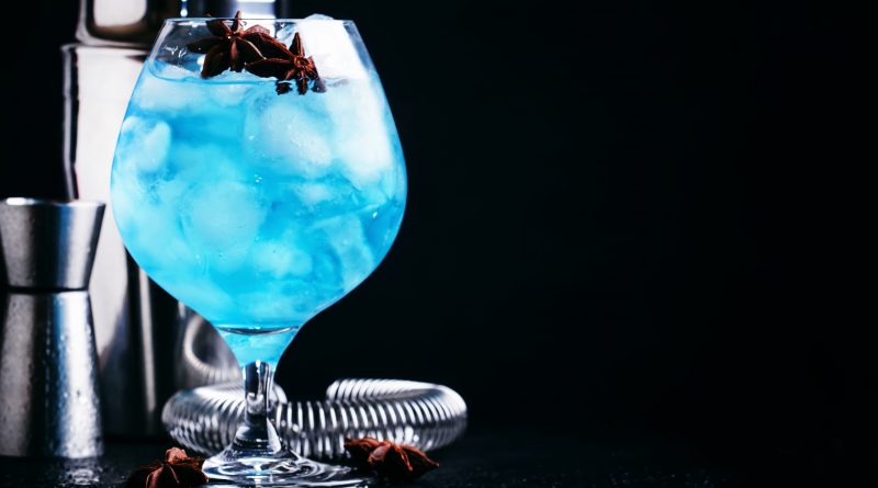 Blue cocktail with ice and anise in brandy glass