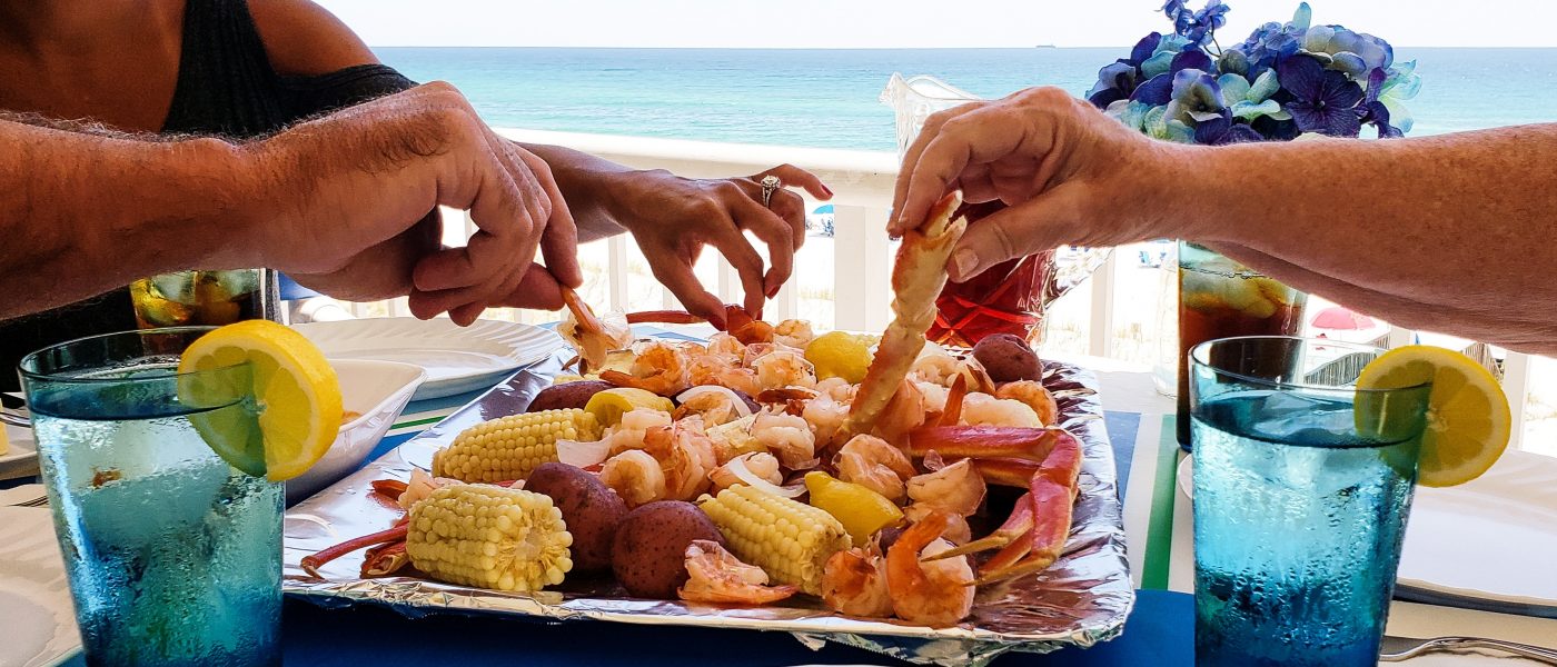 Family fun on beach vacation eating boiled seafood on deck overlooking beach landscape and ocean.