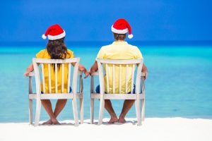 Young couple in Santa hats relaxing on beach during Christmas vacation