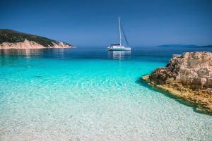 Beautiful azure blue lagoon with sailing catamaran yacht boat at anchor. Pure white pebble beach