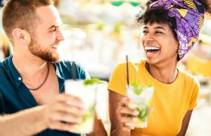 Multicultural trendy couple having fun drinking cocktails at beach party