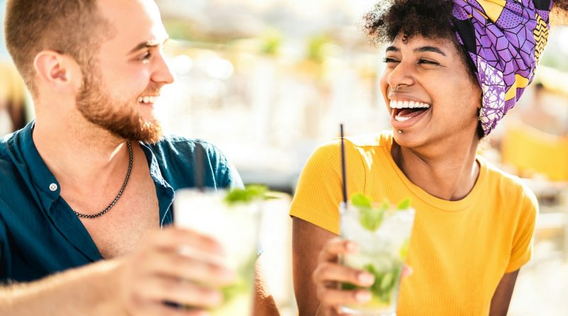 Multicultural trendy couple having fun drinking cocktails at beach party