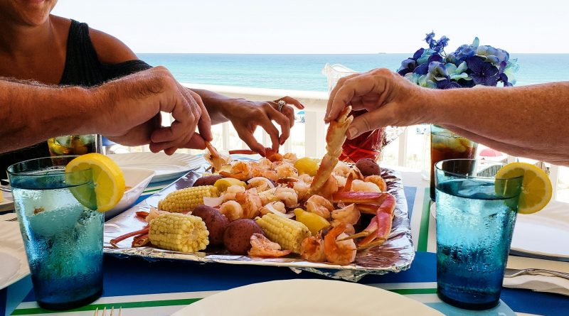 Family fun on beach vacation eating boiled seafood on deck overlooking beach landscape and ocean.