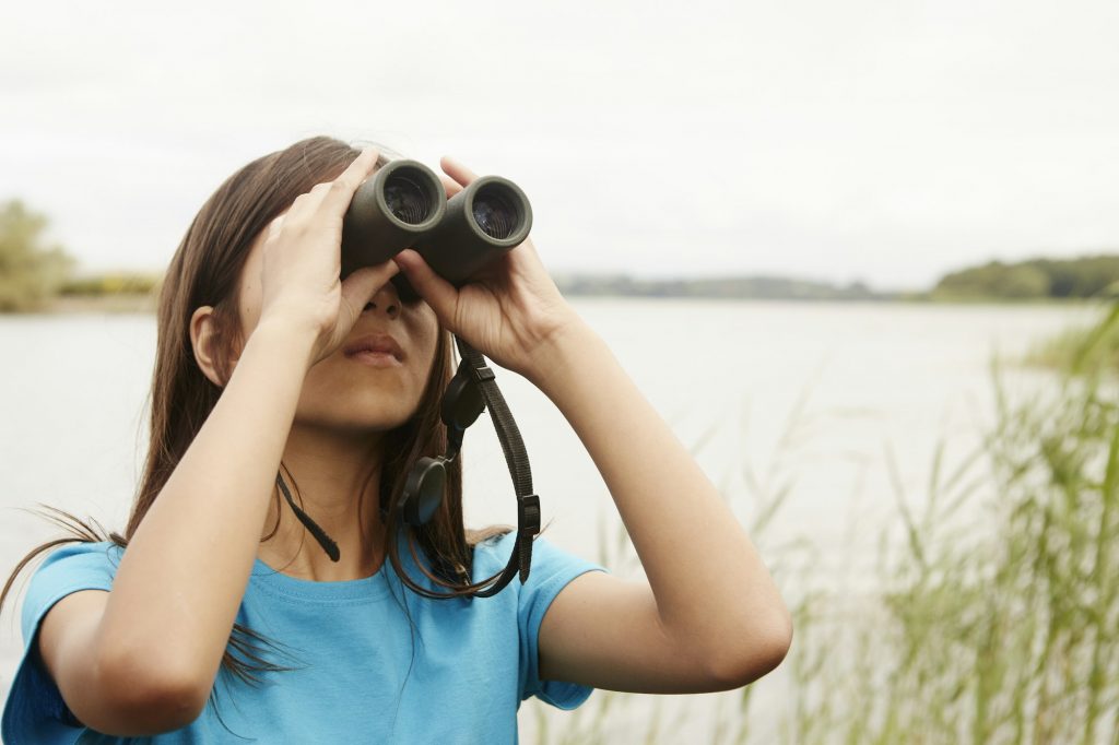 A young girl, a birdwatcher with binoculars.