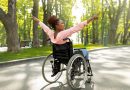 Handicapped black woman in wheelchair on walk at city park, showing victory gesture, feeling